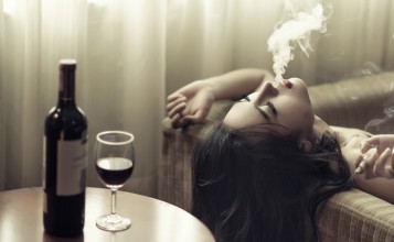 Девушка с сигаретой на диване, бутылка вина и бокал