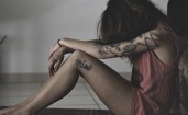 Девушка с татуировками сидит с опущенной головой
