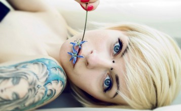 Блондинка с цветком во рту и татуировкой на плече