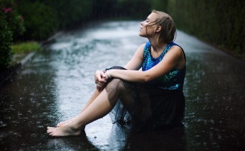 Сидящая на асфальте под дождем девушка