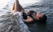 Брюнетка лежит на пляже в воде