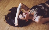 Брюнетка с татуировками лежит на полу
