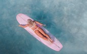 Девушка блондинка на розовом серфе в море