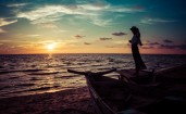Девушка стоит на старой лодке на пляже