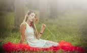 Сидящая на траве девушка нюхает цветок